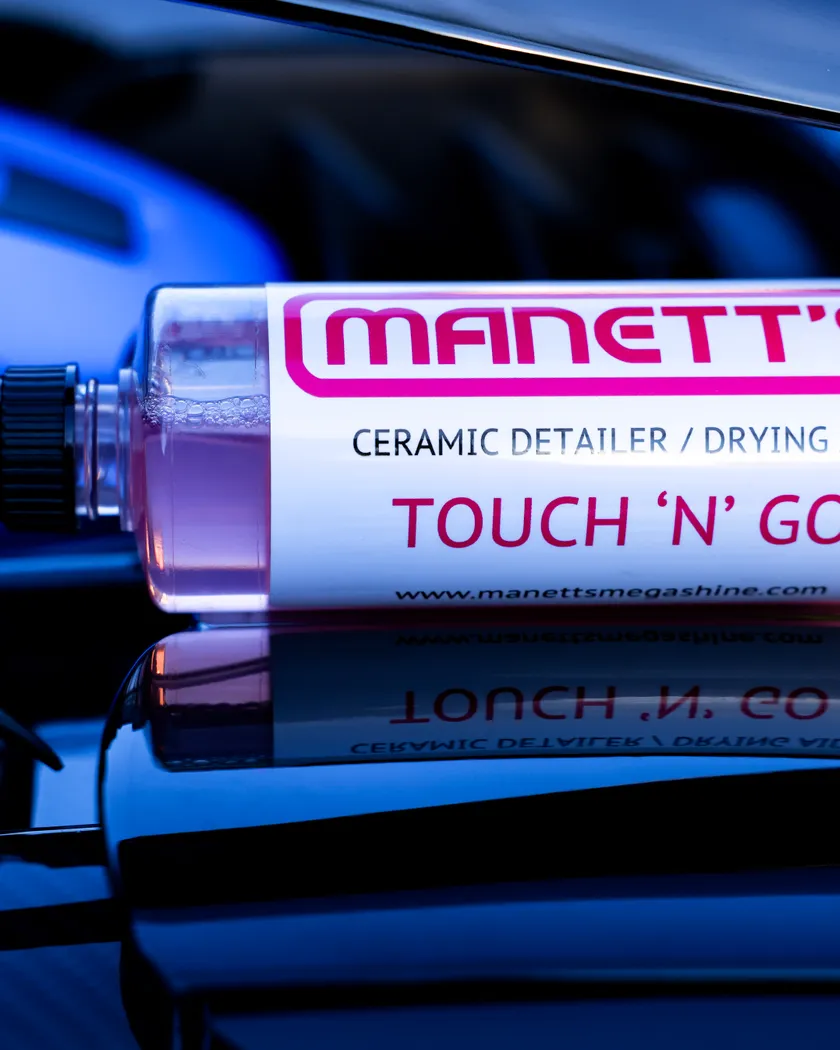 Manetts Touch 'N' Go ceramic detailer and drying aid held beside a vehicle